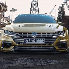 the front end of a yellow volkswagen sedan parked in an industrial area with cranes behind it