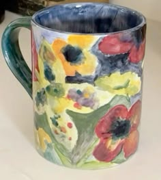 a painted coffee mug sitting on top of a counter next to a vase with flowers