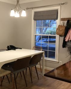 a dining room table with four chairs next to a window and coat rack on the wall