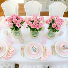 a table set with pink roses in vases and plates