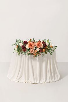 an arrangement of flowers on top of a white table cloth with greenery around it