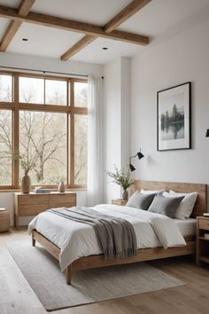 a bedroom with white walls and wood floors, large windows, wooden headboard, two nightstands, and a bed in front of a window