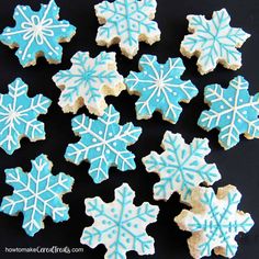 snowflake cookies are arranged on a black surface with white and blue icing