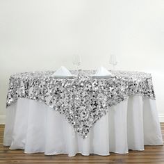 a table with silver sequins on it and white linen draped over the top