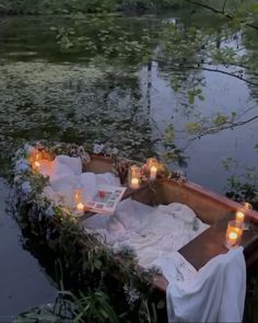 candles are lit in the middle of a row boat on water with flowers and greenery