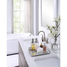 a bathroom sink sitting under a mirror next to a bathtub with flowers in it