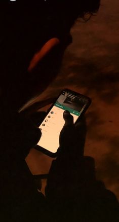 a person holding a cell phone in their hand with the screen lit up at night