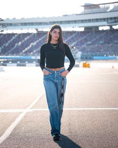 a woman standing on top of a tennis court wearing high waisted jeans and a black crop top