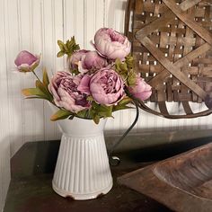 a white vase filled with pink flowers sitting on top of a wooden table next to a basket