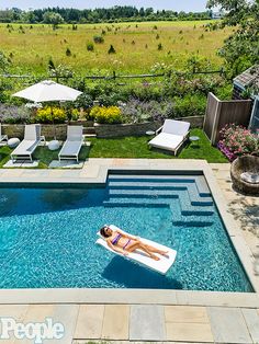 a woman floating in a pool surrounded by lawn chairs and an umbrella on the grass