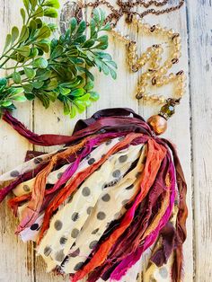 an assortment of scarves and necklaces laid out on a white wooden surface with greenery