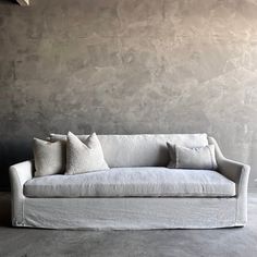 a white couch sitting in front of a wall with two pillows on top of it