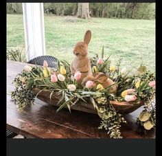 a wooden table topped with a basket filled with flowers and a stuffed rabbit sitting on top of it