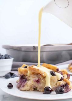 blueberry cobbler being drizzled with white sauce on a white plate