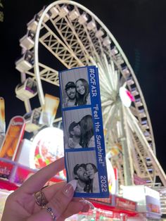 a person holding up a ticket to an amusement park with ferris wheel in the background