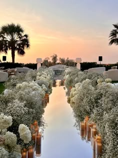 an outdoor ceremony with white flowers and candles on the ground, in front of palm trees