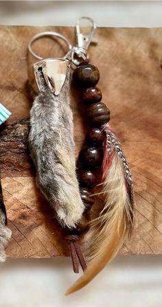 two feathers and beads are on a piece of wood that is being used as a keychain