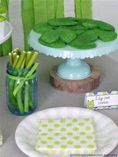 a table topped with green cookies and other food on top of a white plate next to a vase filled with green beans