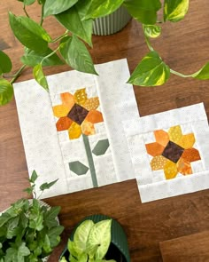 two pieces of quilted paper sitting on top of a wooden table next to a potted plant