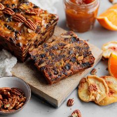 two slices of fruitcake sitting on top of a cutting board next to sliced oranges