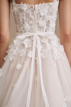 the back of a woman's wedding dress with white flowers and ribbons on it