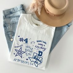 a white shirt with blue writing on it next to jeans and a cowboy's hat