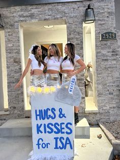 three women in short skirts standing behind a sign that says hugs and kisses for usa