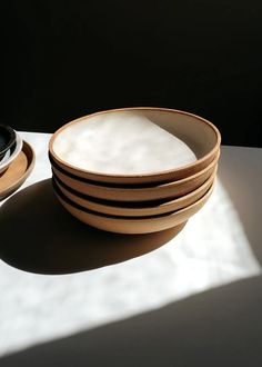 a stack of wooden plates sitting on top of a white table next to a bowl