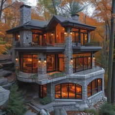 a large stone house in the woods with lots of windows and lights on it's sides