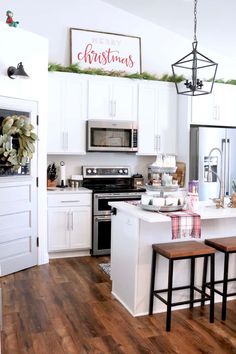 the kitchen is decorated for christmas with white cabinets and wood floors, along with holiday decorations