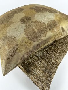 a decorative pillow on top of a white surface with gold and brown circles in the middle