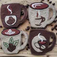 four coffee mug cozies are sitting on a wooden table with coffee beans around them