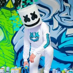 a man in a marshmallow outfit sitting next to cans of sodas with faces painted on them