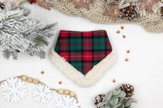 a plaid dog bandana laying on top of snow covered ground next to christmas decorations