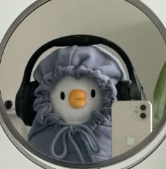 a stuffed penguin with headphones and a cell phone in front of a round mirror