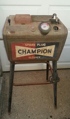 an old gas pump sitting on top of a floor next to a garage door with the word spark plug champion written on it