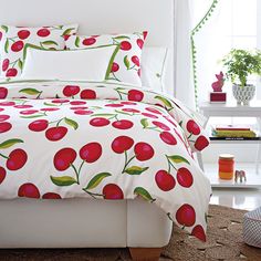 a bed with red cherries on it in a room next to a white wall