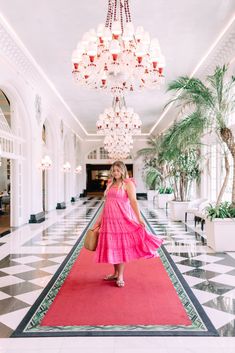 a woman in a pink dress is standing on a red carpet near a chandelier