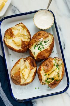 baked potatoes with cheese and chives on a blue tray next to a bowl of mayonnaise