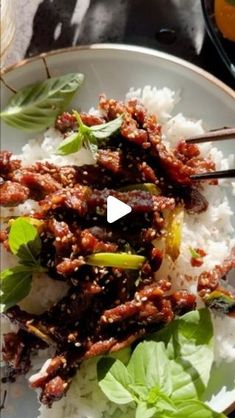 a white plate topped with meat and vegetables on top of rice covered in sauce, garnished with green leaves