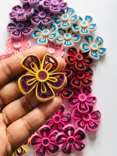 a hand holding a small colorful flower brooch on it's left side, surrounded by smaller colored flowers