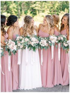 a group of women standing next to each other wearing pink dresses and holding bouquets