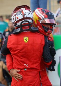 two men in red racing suits hugging each other with helmets on their heads and shoulders