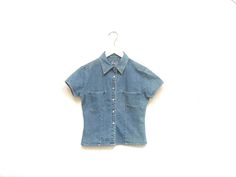 Vintage 90s womens little denim collared shirt. Six pearl snap button closures. Two chest pockets. Short sleeves. Fitted. Southwestern cowgirl bohemian vibes. A wild west top for a adventurous someone. Label: Real Clothes Jeans Fits Like: Marked womens S Color: Medium wash blue denim Fabrication: Cotton denim Condition: Great used condition, normal signs of wear 17" chest 15.5" shoulder 17" length 5" sleeve all measurements taken while garment lying flat This item comes from a pet & smoke free building For a look behind the scenes: + Instagram: brotherxiivintage Fitted Vintage Button-up Denim Top, Medium Wash Fitted Short Sleeve Tops, Fitted Denim Blue Shirt For Summer, Fitted Denim Short Sleeve Top, Fitted Denim Top With Short Sleeves, Fitted Light Wash Tops With Pockets, Vintage Denim Short Sleeve Top, Vintage Short Sleeve Denim Top, Fitted Denim Summer Shirt