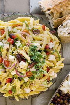 a bowl filled with pasta salad next to bread and olives