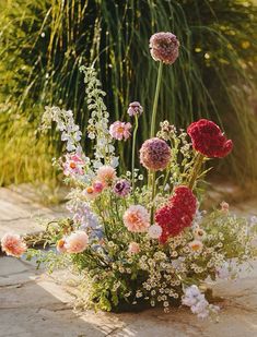 a vase filled with lots of flowers on top of a stone floor next to tall grass