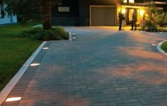 two people standing in front of a house at night with lights on the walkway and driveway