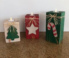 three small wooden boxes with christmas decorations on them, one has a candle in the shape of a stocking