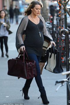 the pregnant woman is walking down the street with her hand on her hip and carrying a purse