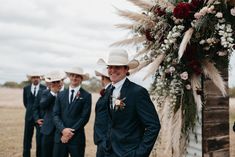 a group of men standing next to each other under a floral covered arch with flowers on it